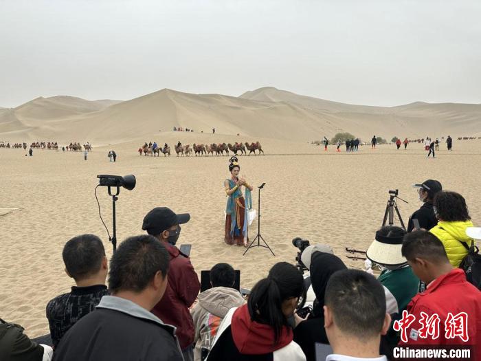 圖為2023年4月底，敦煌大漠“逐舞者”奧楠在鳴沙山月牙泉景區(qū)視頻直播，吸引游人圍觀?！●T志軍 攝
